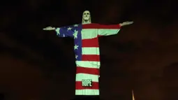 Patung Christ the Redeemer atau patung Yesus sang Penebus yang populer di dunia menyala dengan gambar bendera Amerika Serikat selama pandemi corona Covid-19 di Rio de Janeiro, Brasil, Minggu (12/4/2020). Tubuh patung itu dipenuhi gambar bendera, sekaligus pesan dan harapan. (CARL DE SOUZA/AFP)