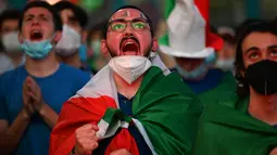 Fans Italia bereaksi ketika mereka menonton di layar raksasa dari zona penggemar resmi di Piazza del Popolo di Roma pada laga pertama grup A Euro 2020 /2021, Jumat (11/6/2021). Timnas Italia berhasil menang 3-0 atas Turki. (ANDREAS SOLARO/AFP)