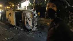 Seorang pemuda berdiri di depan mobil yang telah hangus terbakar saat terjadi bentrokan di kawasan Jalan Diponegoro, Salemba, Jakarta, Kamis (29/3) malam. Sejumlah pengunjuk rasa yang menolak kenaikan harga BBM diamankan, sementara beberapa mahasiswa dan personel kepolisian terluka dalam peristiwa bentrok tersebut. (Antara)