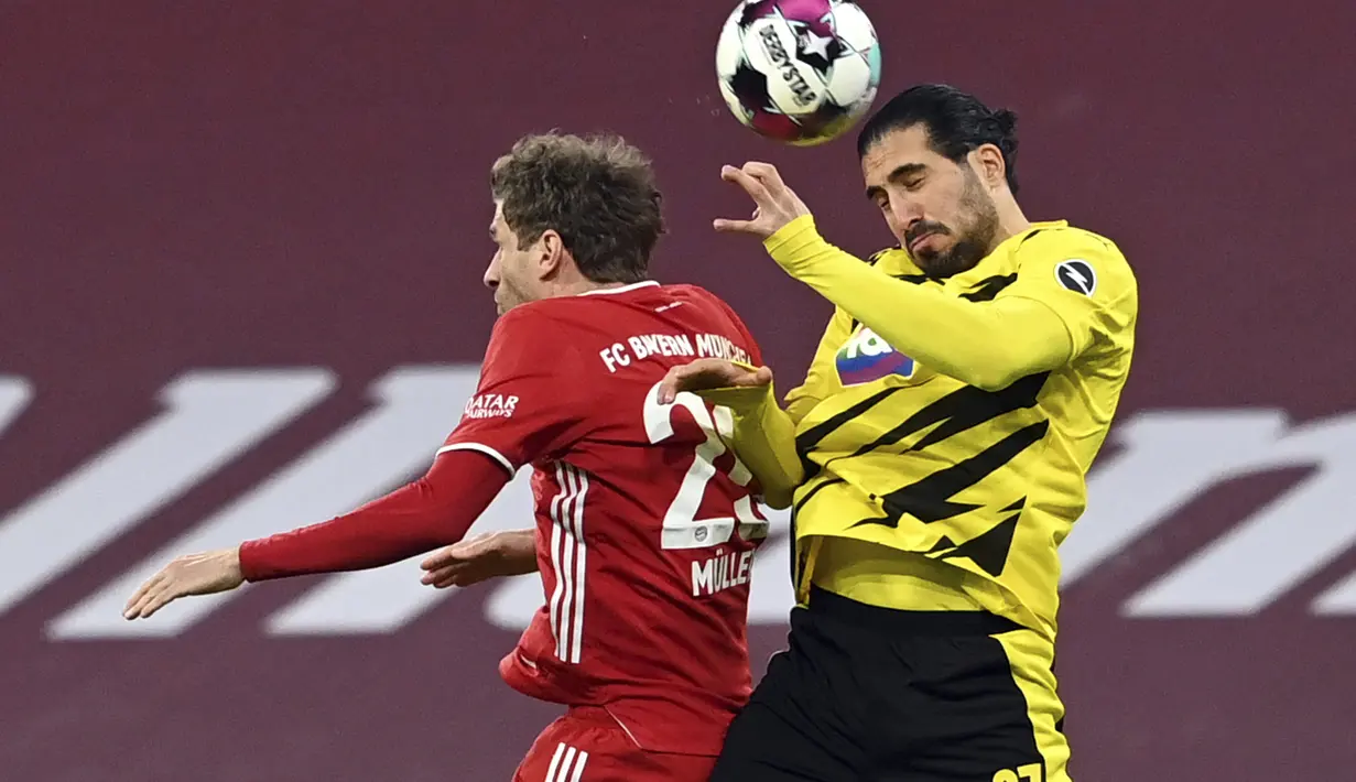 Penyerang Bayern Munchen, Thomas Mueller berebut bola udara dengan gelandang Borrusia Dortmund, Emre Can pada pertandingan lanjutan Bundesliga Jerman di Allianz Arena di Munich, Minggu (7/3/2021). Berkat kemenangan ini Bayern mempertahankan posisi mereka di puncak klasemen. (Sven Hoppe/Pool via AP)