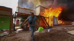 Warga membantu memadamkan api di lingkungan berpenghasilan rendah Laguna Verde, di Iquique, Chili, Senin (10/1/2022). Menurut pihak berwenang, api menghanguskan hampir 100 rumah di lingkungan itu yang sebagian besar dihuni oleh para migran. (AP Photo/Ignacio Munoz)