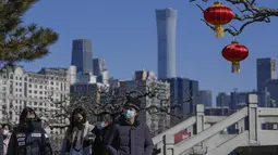 Orang-orang yang memakai masker untuk membantu melindungi dari virus corona berjalan dengan dekorasi lentera jelang Tahun Baru Imlek di sebuah taman di dekat cakrawala kota di Beijing, Kamis (27/1/2022). (AP Photo/Andy Wong)