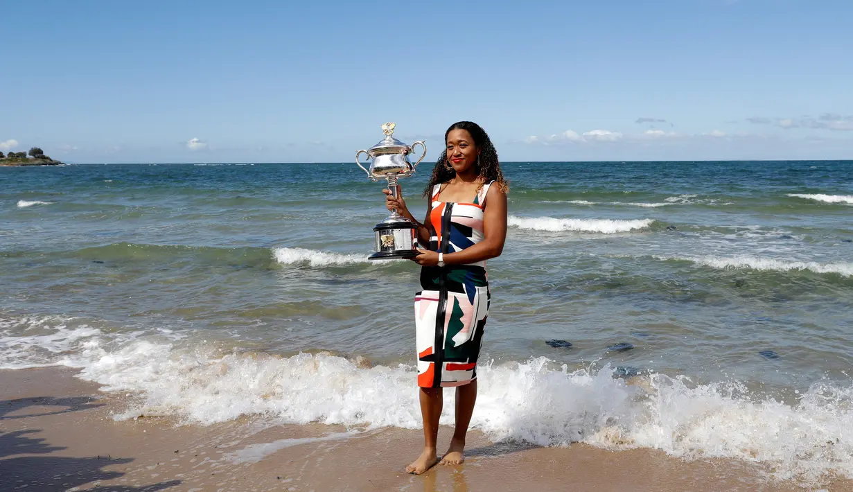 Petenis Jepang, Naomi Osaka menunjukkan trofi juara tunggal putri Australia Terbuka di Pantai Brighton Melbourne, Australia, Minggu (27/1). Prestasi ini membuat Osaka merengkuh gelar Grand Slam secara beruntun. (AP Photo/Kin Cheung)