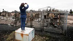 Seorang wanita mengambil foto sisa-sisa kebakaran hutan yang terjadi beberapa hari lalu di kAbasand, Fort McMurray, Alberta, Kanada, (9/5). Kebakaran ini menghanguskan 7.500 hektare lahan. (REUTERS/Chris Wattie)