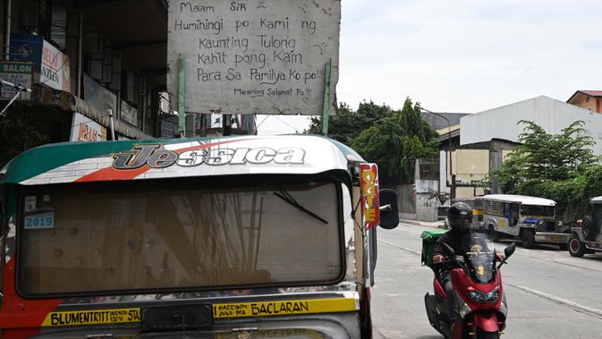 Pengendara motor melewati jeepney milik Daniel Flores yang berfungsi sebagai rumah sementara yang diparkir di Manila, 12 Agustus 2020. Angkutan ikonik di Filipina itu belum dapat mengangkut penumpang sejak Maret akibat lockdown Covid-19 yang membuat jutaan orang kehilangan pekerjaan (Ted ALJIBE/AFP)