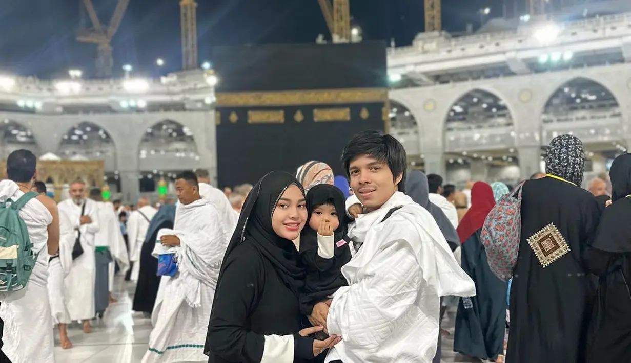 Berpose di depan Ka'bah, ketiga kompak mengenakan outfit hitam-putih. Atta dengan outfit serba putih menggendong Ameena dengan outfit hitam lengkap dengan hijabnya, serasi dengan Aurelie yang juga mengenakan outfit serba hitam. Foto: Instagram.