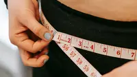 Wanita mengukur lingkar perutnya. (Liputan6.com/Pexels/andres-ayrton)
