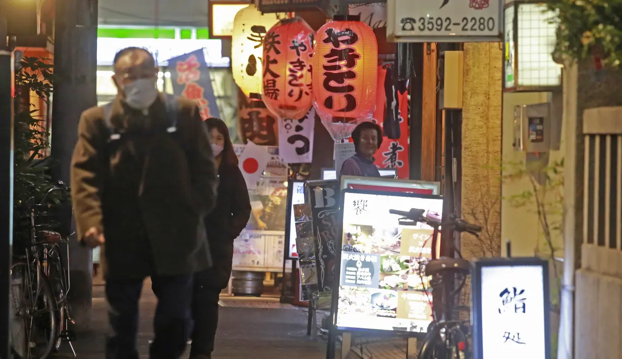 Orang-orang memakai masker untuk melindungi dari penyebaran virus corona berjalan di sepanjang jalan yang dipenuhi bar dan restoran di Tokyo, Rabu (19/1/2022). Para pemimpin lokal mempersingkat jam buka restoran, karena kasus omicron mencapai rekor tertinggi di ibu kota. (AP Photo/Koji Sasahara)