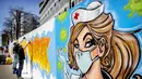Seniman jalanan Jim Haan membuat mural di pagar konstruksi markas NL Dutch Post NL di Den Haag, Belanda, Jumat (10/4/2020). Seniman jalanan Belanda membuat mural untuk mendukung mereka yang berjuang selama pandemi virus corona COVID-19. (Koen Van WEEL/ANP/AFP)