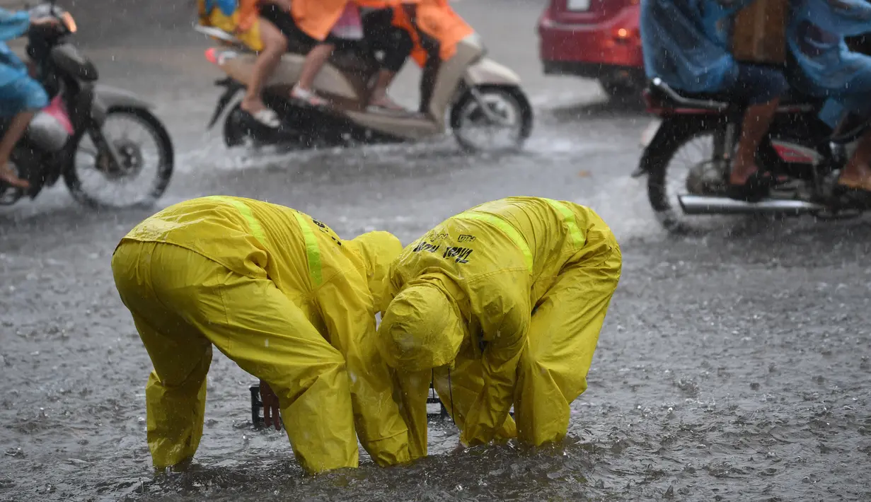 Dua petugas kota membuka selokan di jalan yang banjir setelah badai tropis Talas terjadi di Hanoi, Vietnam utara (17/7). Kondisi cuaca ini disebabkan adanya Badai Talas di perairan Laut Cina Selatan. (AFP Photo/Hoang Dinh Nam)