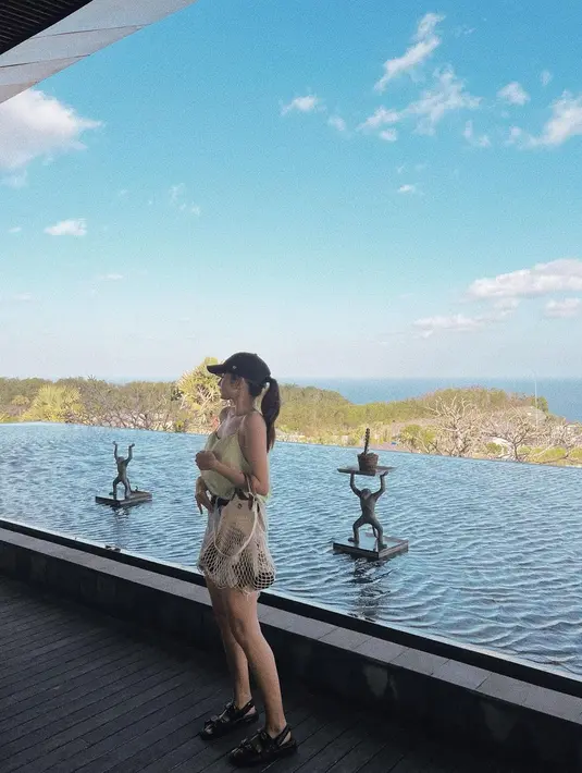 Dalam foto ini, Enzy memakai tanktop berwarna green sage yang dituck-in ke celana pendek berwarna putih. Dia juga menambahkan aksesori topi berwarna hitam dan tas fishnet bag. Dia terlihat berpose di pinggir kolam renang. (Instagram/enzystoria)