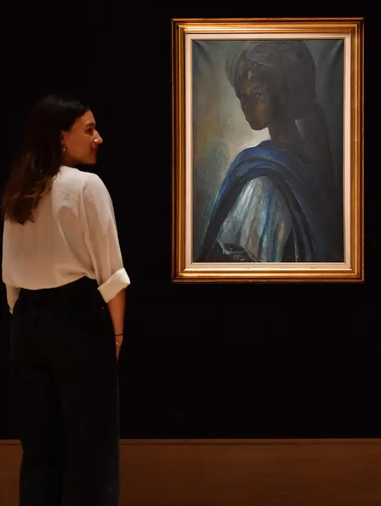 Karyawan rumah lelang Bonhams berdiri dekat lukisan seorang putri Nigeria bernama Tutu di London pada 7 Februari 2018. Mona Lisa dari Afrika itu sempat hilang bertahun-tahun sebelum ditemukan di apartemen London belum lama ini. (BEN STANSALL/AFP)