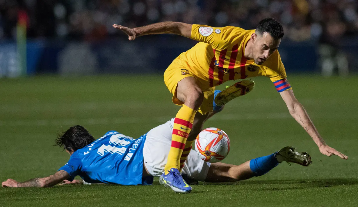 Gelandang Linares Deportivo, Fran Carnicer (kiri) berebut bola dengan gelandang Barcelona Sergio Busquets pada babak 32 Besar Copa del Rey di Estadio Linarejos, Kamis (6/1/2022) dini hari WIB. Barcelona susah payah menang 2-1 atas tim divisi 3 Linares Deportivo. (JORGE GUERRERO / AFP)