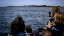 Turis mengambil gambar lumba-lumba berenang di Tagus melewati perahu pengamat spesies laut di lepas pantai Lisbon, Portugal pada 7 Agustus 2021. Lalu lintas laut yang berkurang akibat pandemi corona membuat ekosistem di Sungai Tagus kembali ramah untuk lumba-lumba. (PATRICIA DE MELO MOREIRA / AFP)