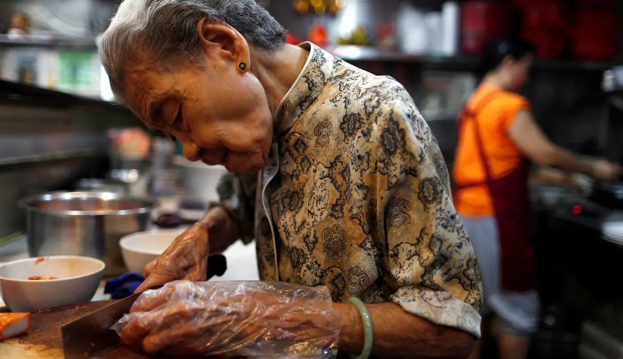 Nenek Leong Yuet Meng memotong daging babi di warungnya di Singapura (22/3). Nenek Leong turun langsung dengan dibantu beberapa asistennya untuk membuat mie pangsit dan menyajikannya di atas mangkuk. (Reuters/Edgar Su)