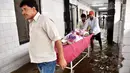 Seorang pasien dipindahkan melewati koridor rumah sakit yang tergenang banjir di Nalanda Medical College Hospital, daerah Bihar, India, 29 Juli 2018. Rumah sakit itu digenangi air kotor dengan sejumlah ikan terlihat berenang memenuhi lantai. (AFP PHOTO)