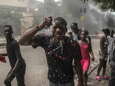 Seorang pengunjuk rasa yang terkena gas air mata polisi memercikkan air ke wajahnya, selama protes menuntut Perdana Menteri Haiti Ariel Henry mundur dan menyerukan kualitas hidup yang lebih baik, di Port-au-Prince, Haiti, Senin (29/8/2022). (AP Photo/Odelyn Joseph)