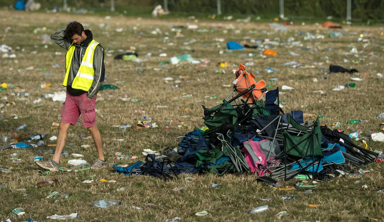 Seorang pria melewati kursi lipat dekat Pyramid Stage pada akhir Festival Glastonbury di arena Worthy Farm, Inggris, 26 Juni 2017. Penyelenggaraan festival musik terbesar di dunia itu menyisakan sampah yang berserakan di seluruh arena. (OLI SCARFF/AFP)