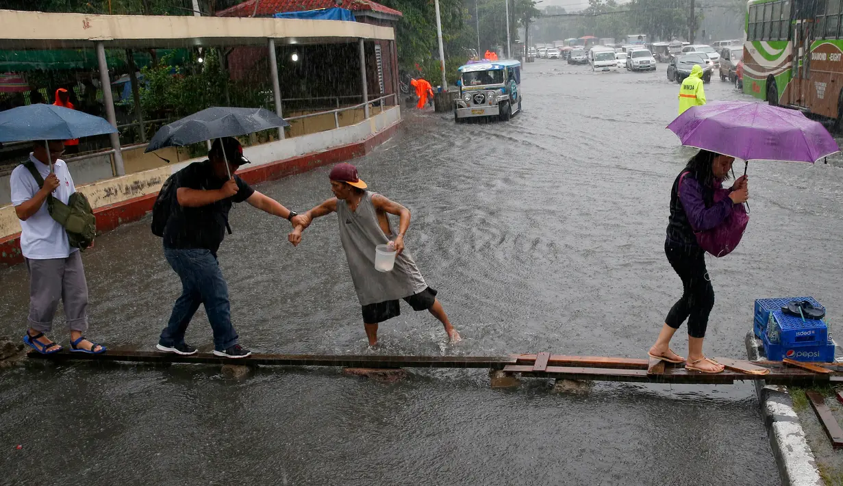 Seorang kernet (tengah) membantu penumpangnya menyebrangi genangan air di Manila, Filipina, Kamis (27/7). Pihak Atmosfer, Geofisika dan Astronomi Filipina (PAGASA) membenarkan adanya badai tropis ‘Nesat’ di timur laut Filipina. (AP/Bullit Marquez)