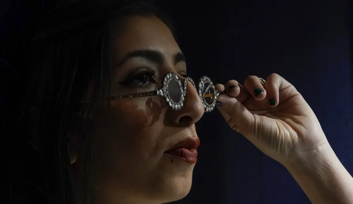 Seorang anggota staf mengenakan kacamata Mughal dengan lensa berlian, dalam bingkai berlian, di Sotheby's, di London, Jumat (22/10/2021). Kacamata adalah contoh yang sangat langka dari kerajinan perhiasan Mughal. (AP Photo/Alberto Pezzali)