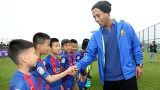 Pemain sepak bola asal Brasil, Ronaldinho bersalaman dengan pemain bola cilik di China (24/2). Mantan pemain klub Spanyol, Barcelona itu menghadiri peresmian berdirinya akademi sepak bola Barcelona di China. (Handout / Mission Hills / AFP)