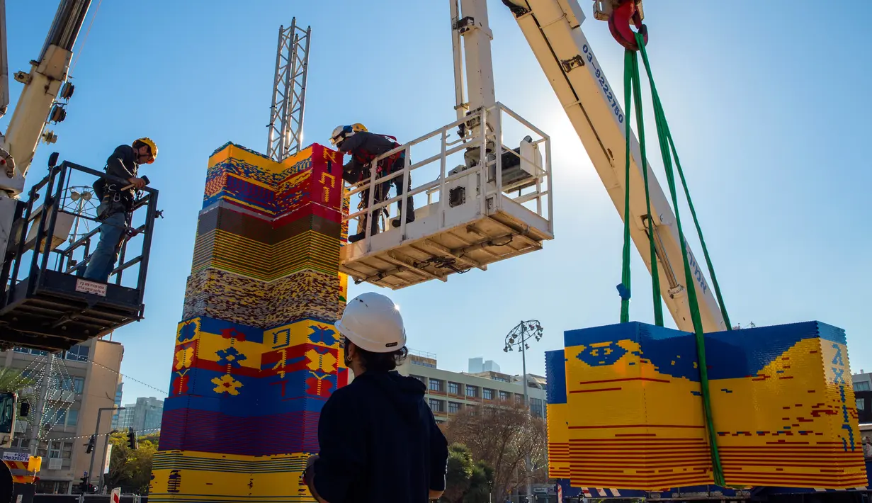 Pekerja dan relawan menggunakan alat berat saat menyusun kepingan LEGO untuk membuat menara di Lapangan Rabin di Tel Aviv, Israel, Rabu (27/12). Menara LEGO ini juga dibuat untuk memecahkan Guinness World Record. (AFP Photo/Jack Guez)