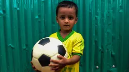 Seorang anak Rohingya mengenakan jersey timnas Brasil sambil memegang bola di kamp pengungsi Kutupalong di Ukhia, Bangladesh, 19 Juli 2018. Bagi pengungsi anak-anak Rohingya, Piala Dunia 2018 ini adalah ajang pertama bagi mereka. (AFP/Munir UZ ZAMAN)