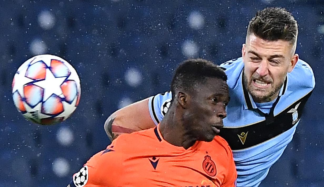 Gelandang Lazio, Sergej Milinkovic-Savic, berebut bola dengan bek Club Brugge, Odilon Kossounou, pada laga Grup F Liga Champions di Olympic Stadium, Rabu (9/12/2020) dini hari WIB. Lazio bermain imbang 2-2 melawan Club Brugge. (AFP/Tiziana Fabi)