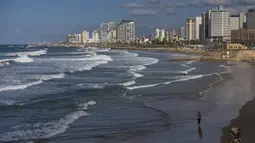 Seorang perempuan berjalan di tepi pantai Laut Mediterania Tel Aviv, Israel, Kamis (2/12/2021). Economist Intelligence Unit (EIU) pada 1 Desember mengumumkan Tel Aviv telah menggeser posisi Paris sebagai kota termahal di dunia untuk ditinggali. (AP Photo/Oded Balilty)
