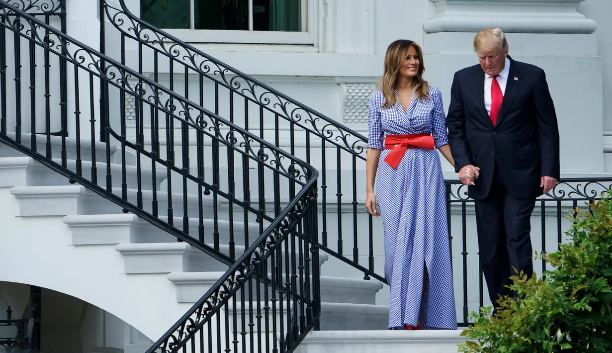 Presiden AS Donald Trump menggandeng tangan Melania sambil menuruni tangga menyambut keluarga militer pada acara piknik di Gedung Putih, Rabu (4/7). Pasangan yang jarang bergandengan di depan umum itu langsung mencuri perhatian. (AFP/Brendan Smialowski)