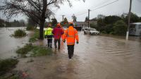 Petugas melintasi banjir untuk mengevakuasi pemilik rumah di Christchurch, Selandia Baru, Sabtu, (22/7). Dewan Kota Christchurch mengatakan keadaan darurat setelah Sungai Heathcote meluap akibat cuaca yan buruk. (AP Photo / Mark Baker)