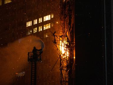 Seorang petugas pemadam kebakaran menyemprotkan air ke api di Hong Kong, Jumat (3/3/2023). Petugas pemadam kebakaran Hong Kong sedang memadamkan kobaran api yang terjadi di lokasi konstruksi di distrik perbelanjaan populer kota itu. (AP Photo/Louise Delmotte)