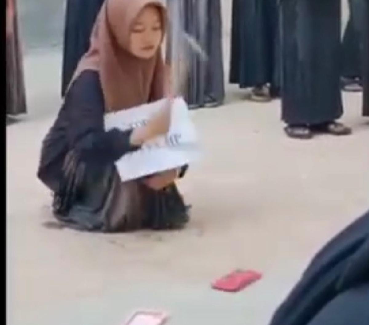 Sebagai hukuman, santriwati ini harus menghancurkan hpnya sendiri. <br><br>Berjongkok, santriwati ini terlihat membawa palu untuk menghancurkan hp miliknya.