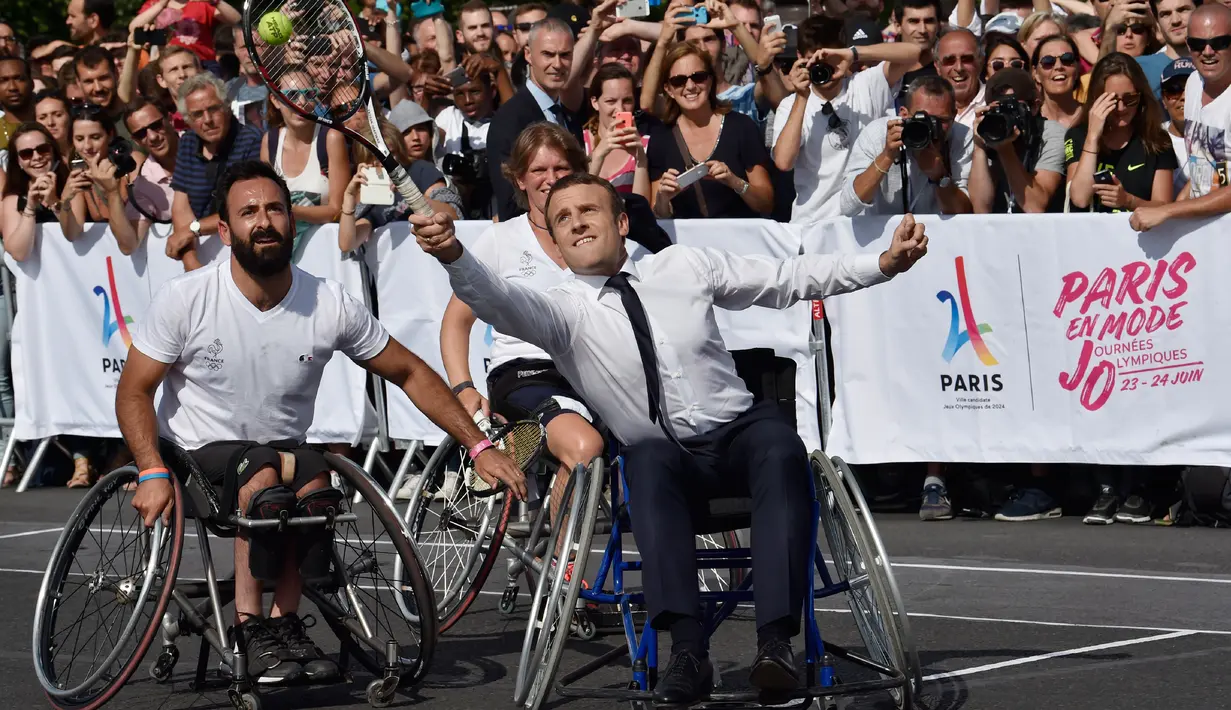 Presiden Prancis Emmanuel Macron berusaha memukul bola sambil duduk di kursi roda di Paris, Prancis (24/6). Kegiatan ini sebagai bentuk promosi Paris untuk menjadi kandidat tuan rumah Olimpiade dan Paralimpiade 2024. (AFP Photo/Alain Jocard)
