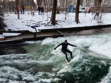 Seorang pria menaklukkan ombak saat berselancar di Sungai Eisbach selama hari musim dingin di Munich, Jerman, 4 Januari 2017. Eisbach merupakan sungai buatan dengan panjang dua kilometer dan arusnya pun merupakan buatan. (Mark RALSTON/AFP)