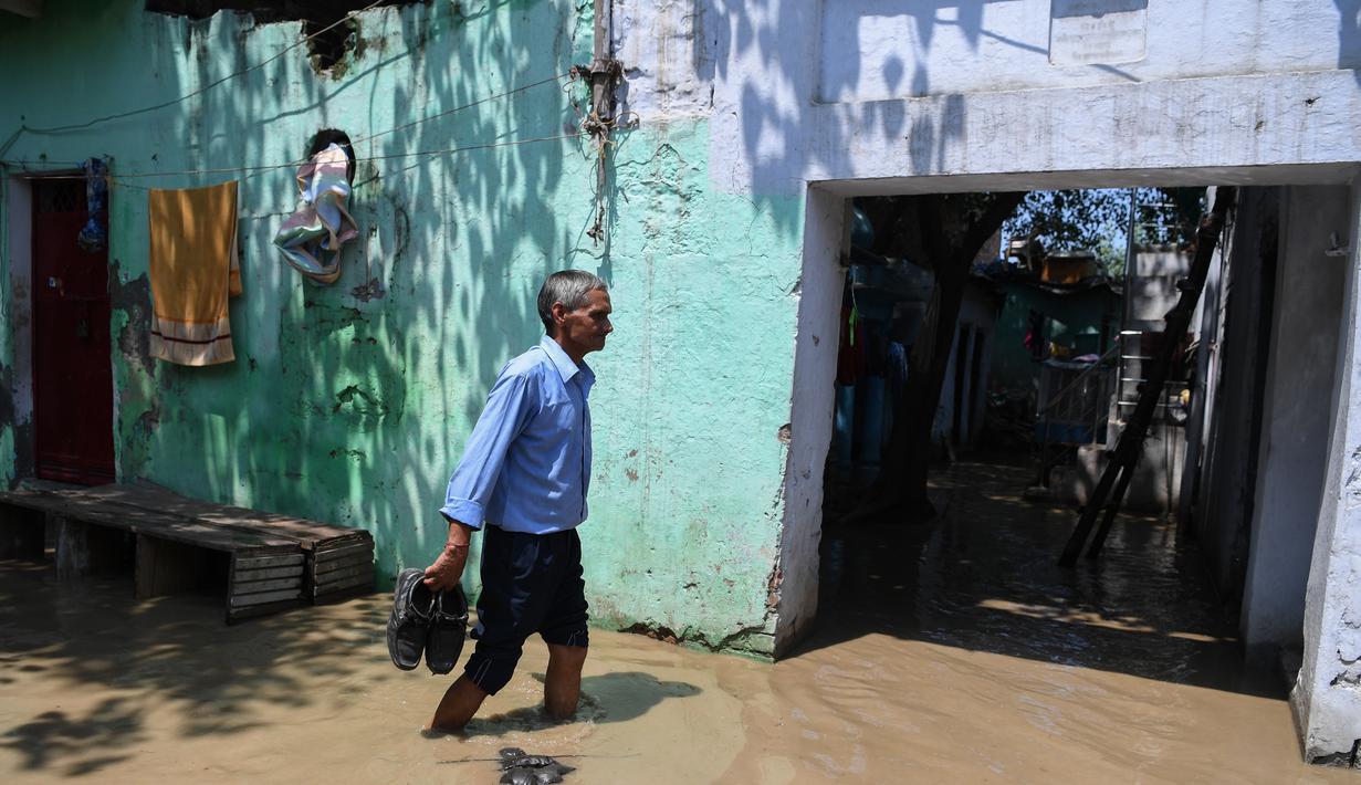 Seorang pria membawa sepatunya saat melintasi banjir di daerah perumahan dekat tepi Sungai Yamuna yang meluap di New Delhi, India, Selasa (20/8/2019). (AFP Photo/Sajjad Hussain)