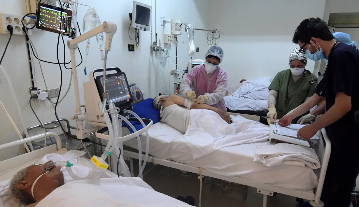 Petugas medis Tunisia merawat pasien di gym yang diubah untuk menangani lonjakan infeksi COVID-19 di pusat kota Kairouan pada 4 Juli 2021. Tunisia tengah berjuang menghadapi tsunami COVID-19 sementara jumlah orang yang meninggal akibat virus corona terus melonjak tinggi. (FETHI BELAID/AFP)