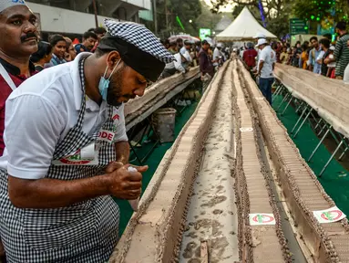 Seorang tukang roti menyelesaikan kue sepanjang 6,5 km untuk kue terpanjang dunia, di Thrissur di negara bagian Kerala, India selatan (15/1/2020). Ratusan pembuat roti dan koki di India selatan membuat kue terpanjang di dunia. (AFP/Arun Sankar)