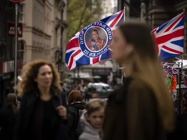 Pejalan kaki berjalan melewati kios yang menjual bendera yang mengumumkan penobatan Raja Charles di London, Jumat, 5 Mei 2023. Penobatan Raja Charles III akan berlangsung di Westminster Abbey pada 6 Mei. (AP Photo/Emilio Morenatti)