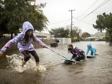 Anak-anak bermain di genangan air di Mill Valley, California, Minggu (24/10/2021). Badai kuat menerjang California Utara yang sempat mengalami kebakaran hutan, memicu tanah longsor dan banjir, juga membawa angin kencang yang merobohkan tiang-tiang listrik serta pohon tumbang. (AP Photo/Ethan Swope)