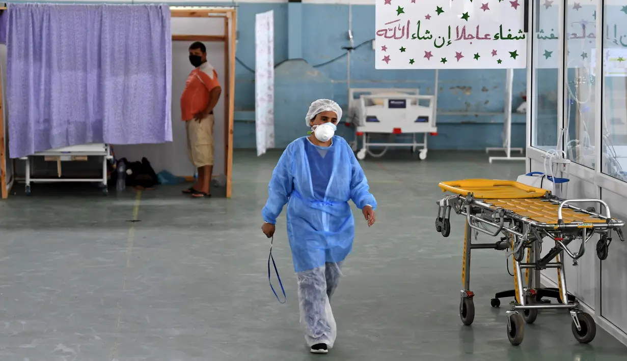Seorang dokter Tunisia merawat seorang pasien di gym yang diubah untuk menangani lonjakan infeksi COVID-19 di pusat kota Kairouan pada 4 Juli 2021. Tunisia tengah berjuang menghadapi tsunami COVID-19 sementara jumlah orang yang meninggal akibat virus corona terus melonjak tinggi. (FETHI BELAID/AFP)