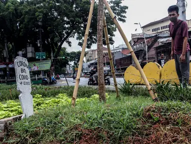 Warga melihat kuburan dengan papan nisan bertuliskan Corona bin Covid di taman Jalan Jatinegara Barat, Jakarta, Minggu (20/9/2020). Kuburan tersebut sengaja dibuat untuk mengingatkan masyarakat yang melintas akan bahaya virus Covid-19. (Liputan6.comm/Johan Tallo)