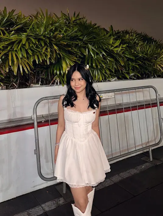 Hanggini mengenakan puffy dress putih dengan boots warna senada. Penampilannya yang manis ini bisa masuk era Folklore dan Lover karena jepitan kupu-kupu yang dipakainya. [@hanggini]