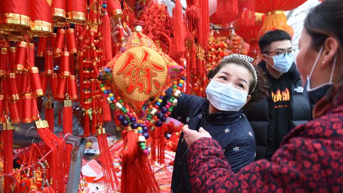 Orang-orang mengenakan masker saat berbelanja dekorasi untuk perayaan Imlek Tahun Tikus Logam di sebuah pasar di Provinsi Anhui, China, 24 Januari 2020. Otoritas China dengan cepat membangun rumah  sakit yang didedikasikan untuk merawat pasien yang terjangkit virus corona. (Chinatopix via AP)