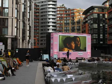 Orang-orang duduk menonton film pada layar lebar saat acara pratinjau bioskop apung di Merchant Square di Kanal Regent, London, Rabu (1/9/2020). Bioskop bernama Openaireini itu memberi dua pilihan tempat duduk kepada penonton, yakni duduk di perahu atau di kursi di tepi kanal. (ISABEL INFANTES/AFP)