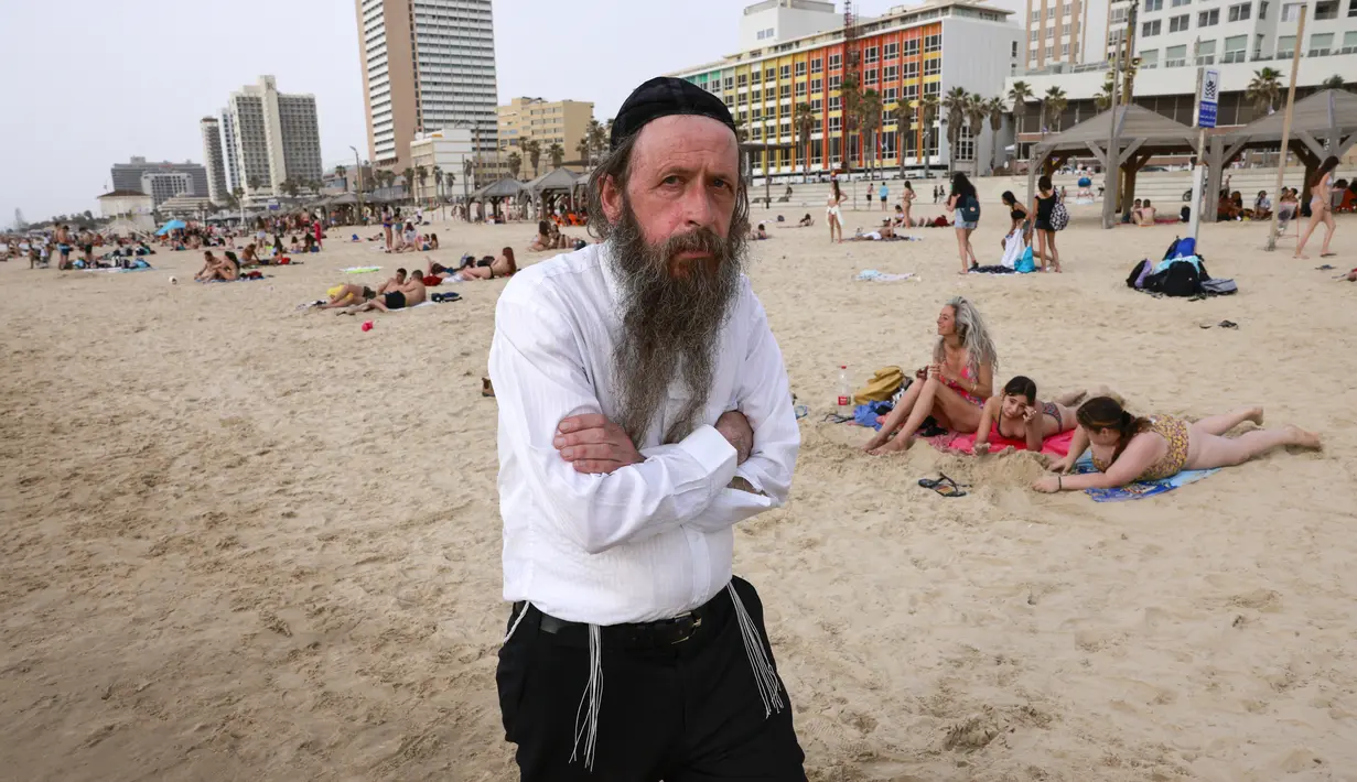 Seorang pria Yahudi Ultra-Ortodoks berjalan di pantai di kota pesisir Israel Tel Aviv (19/4/2021). Pemerintah Israel mencabut kewajiban memakai masker setelah 81 persen penduduk dewasa menerima vaksin Covid-19. (AFP/menahem kahana)