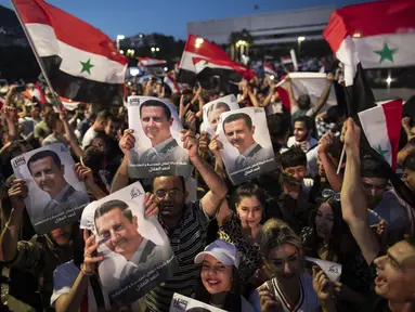 Pendukung mengibarkan bendera nasional dan foto Presiden Suriah Bashar Assad saat mereka merayakan kemenangannya di Omayyad Square, di Damaskus, Kamis (27/5/2021). Bashar al-Assad terpilih kembali untuk masa jabatan keempat sebagai presiden Suriah yang dilanda perang. (AP Photo/Hassan Ammar)