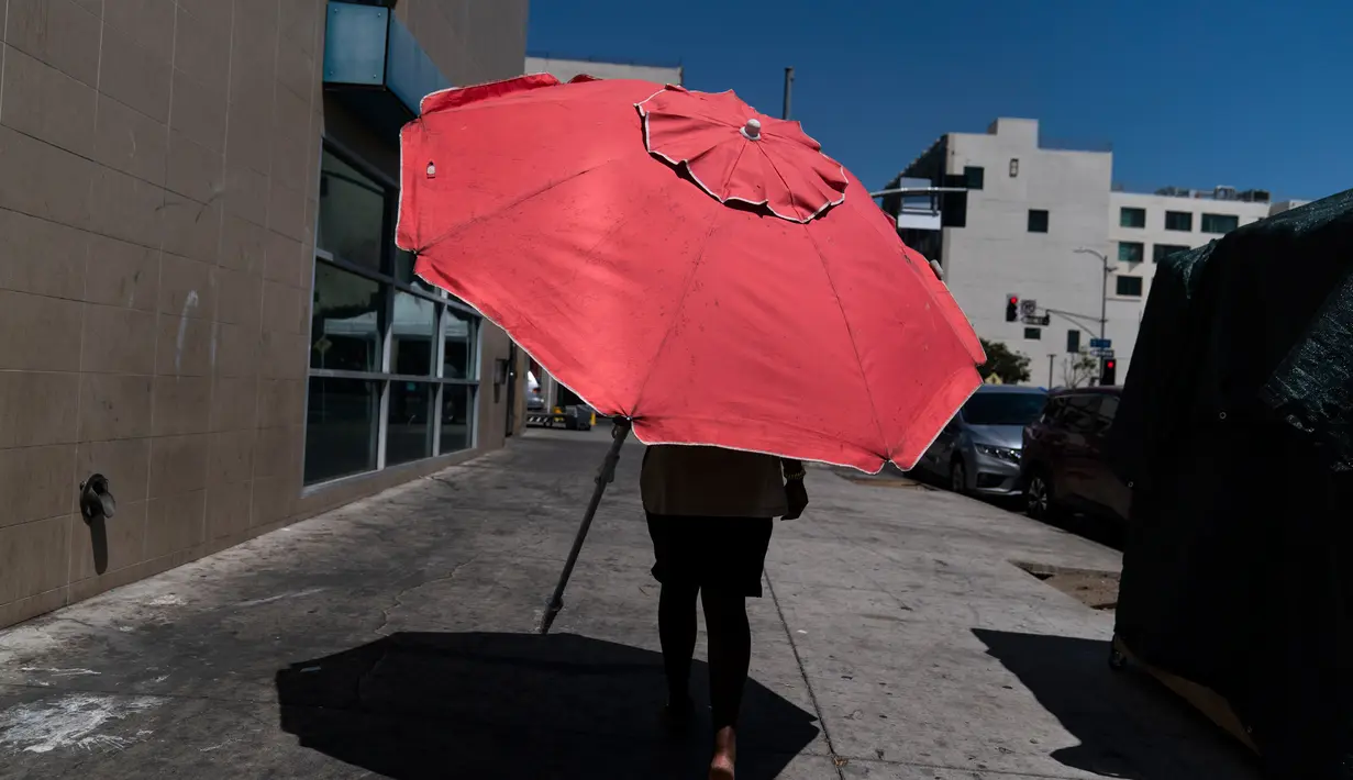 Seorang wanita berjalan dengan payung pantai di Los Angeles, Rabu, (31/8/2022). Peringatan panas berlebihan meluas ke seluruh California Selatan dan ke utara, beberapa kota California memecahkan rekor panas, naik setinggi 112F, dan kobaran api meletus saat penduduk terpaksa mengungsi. (AP Photo/Jae C.Hong)