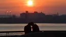 Pasangan mengobrol saat matahari terbenam di Liverpool Pier Head, Liverpool, Inggris, 26 Maret 2020. Organisasi Kesehatan Dunia (WHO) mengumumkan virus corona COVID-19 sebagai pandemi sejak 11 Maret 2020 lalu. (Paul ELLIS/AFP)