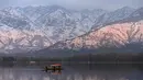 Orang-orang menikmati perjalanan dengan perahu dengan latar belakang pegunungan yang tertutup salju di danau Dal di Srinagar (11/1/2022). Danau Dal yang merupakan danau terbesar kedua di propinsi Jammu dan Kashmir negara bagian India ini merupakan pusat pariwisata dan rekreasi. (AFP/Tauseef Mustafa)